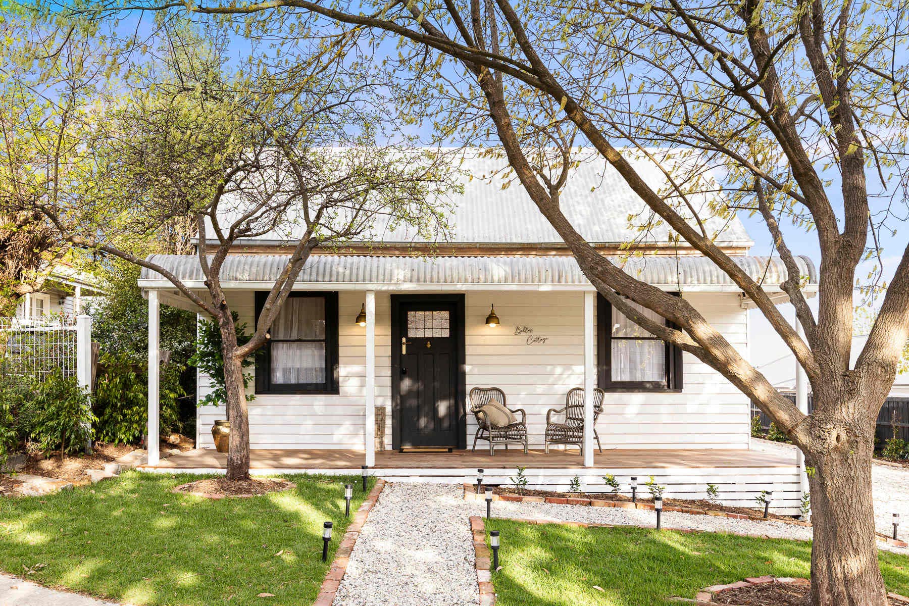 Bella's Cottage, a white weatherboard cottage with a front porch among trees