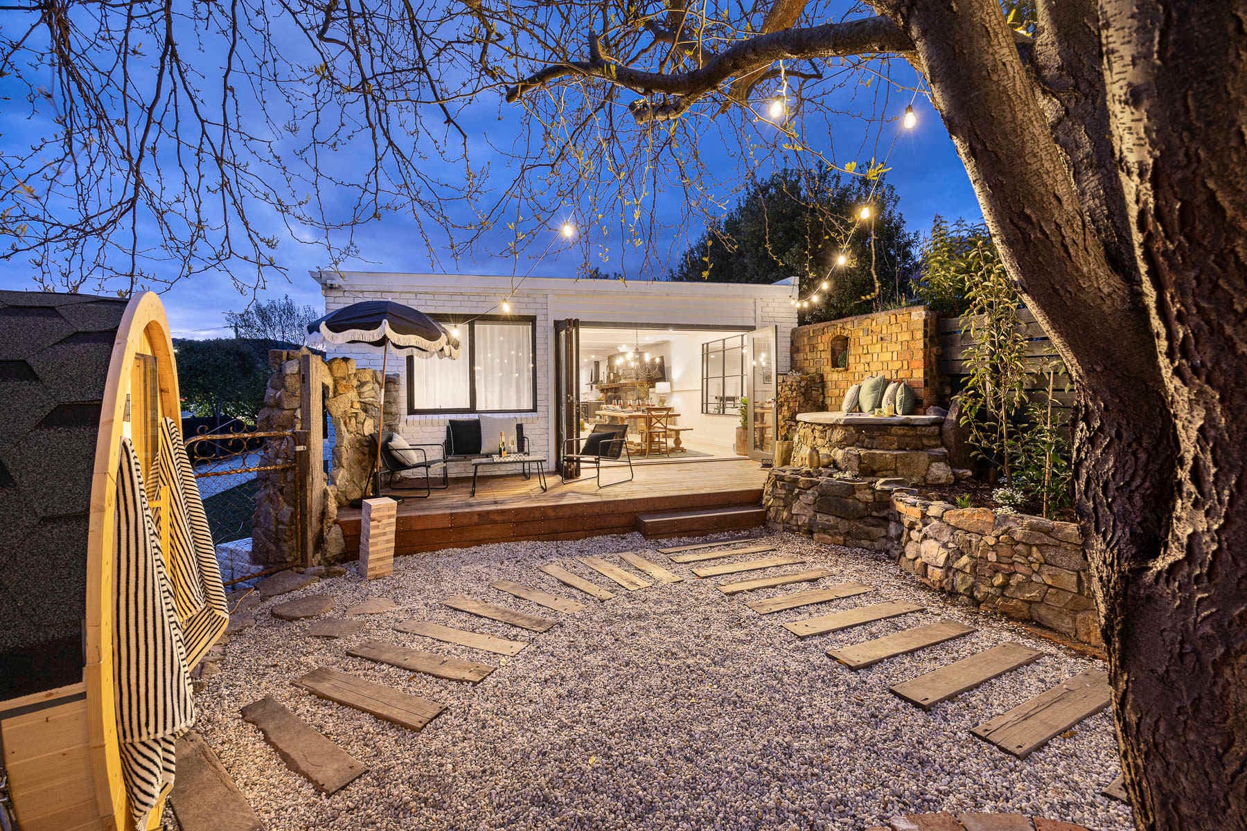 The garden at Bella's Cottage at dusk, with a barrel sauna, stepping stones and the lit deck