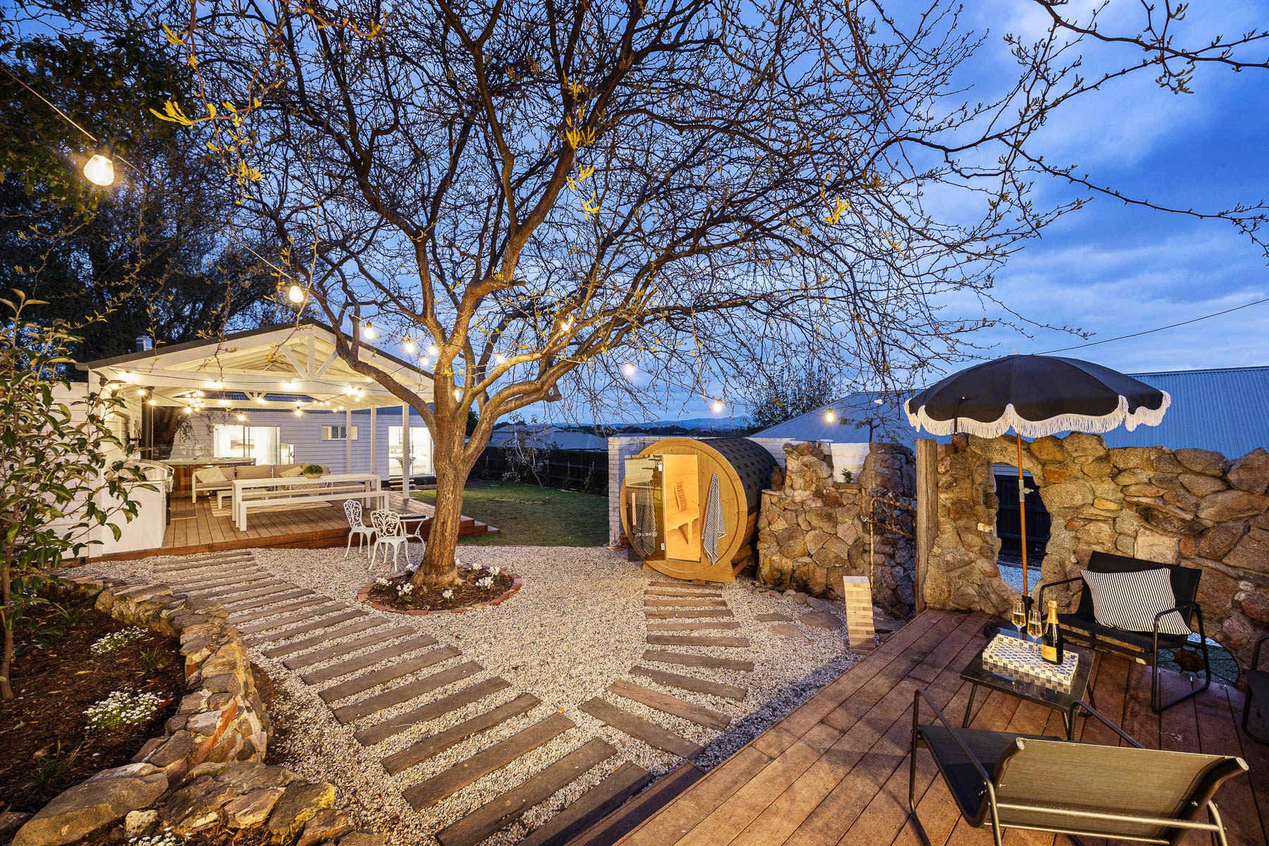 The courtyard at Bella's Cottage at dusk, with fairy lights, stepping stones and a barrel sauna