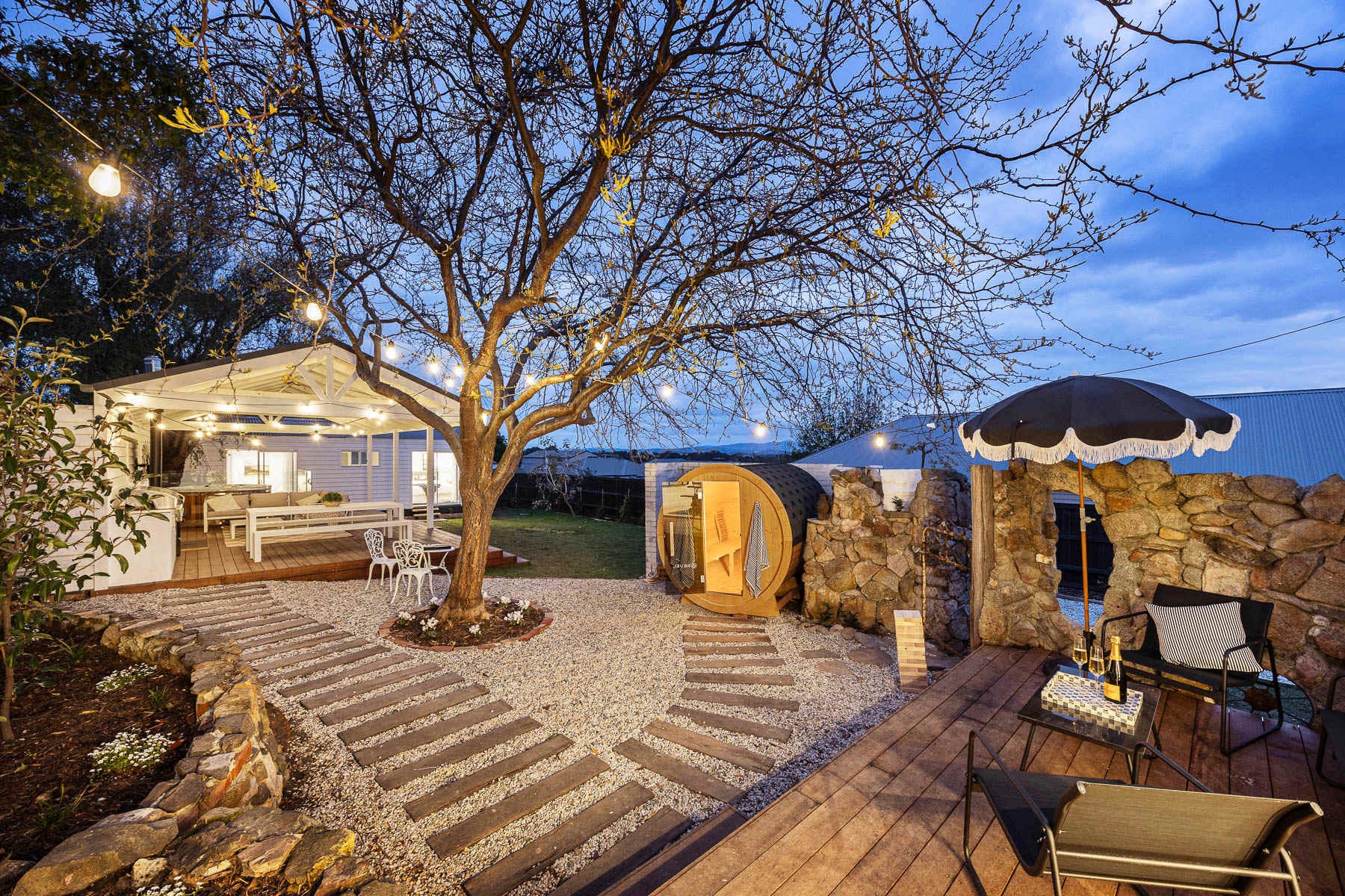 Courtyard at Bella's Cottage in Yarra Glen at dusk, with a barrel sauna beside the stone wall