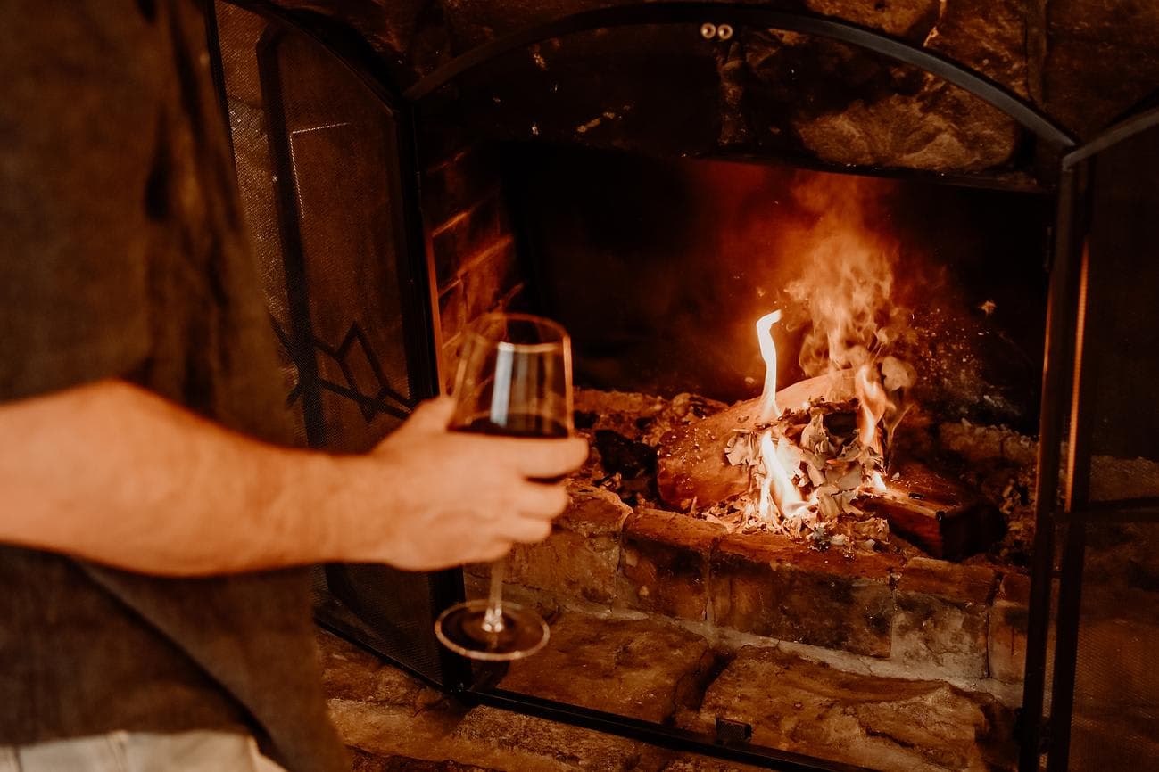 A glass of red wine held beside a log fire