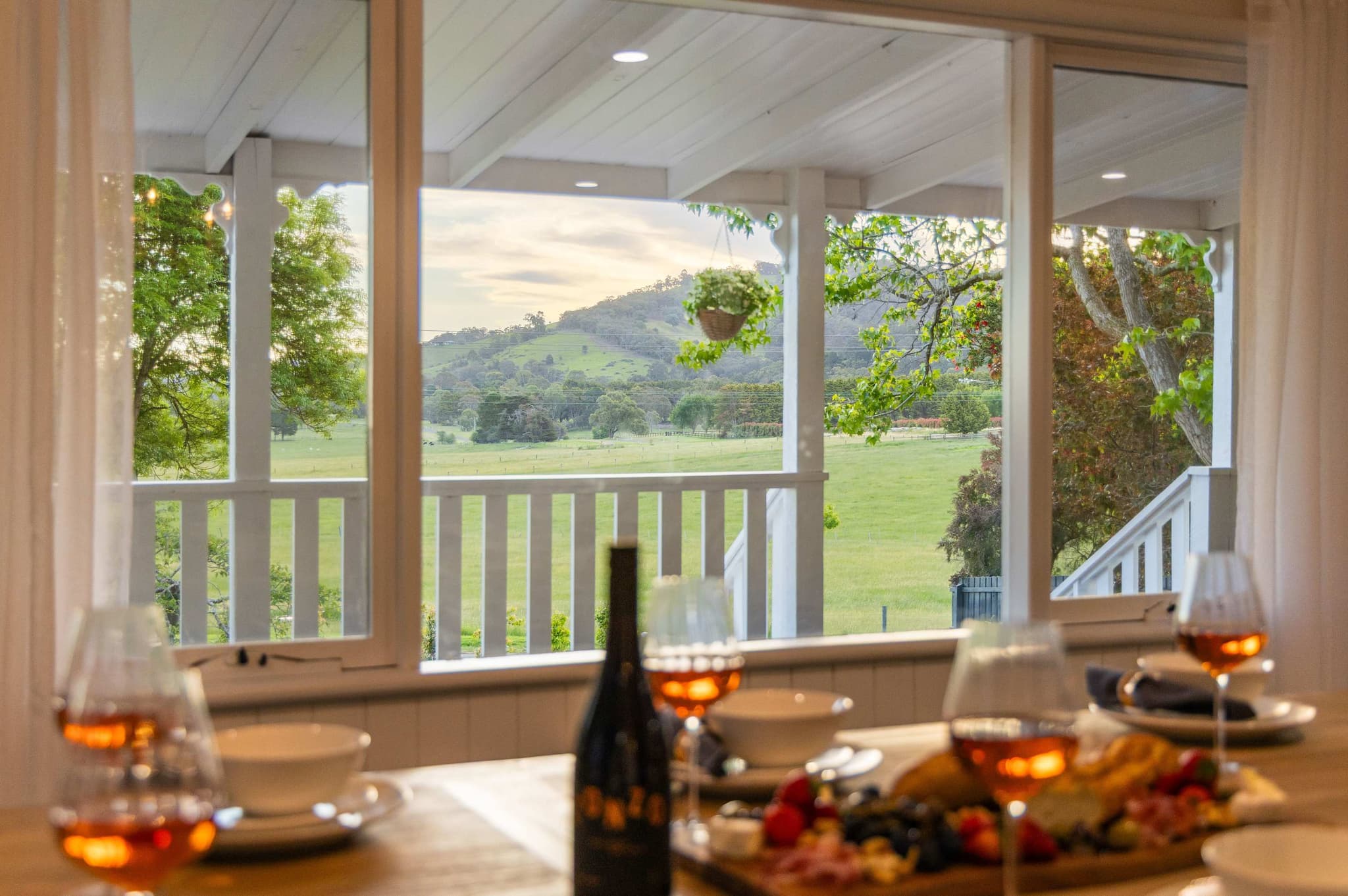 Wine glasses and a grazing board at a window with paddocks and hills beyond