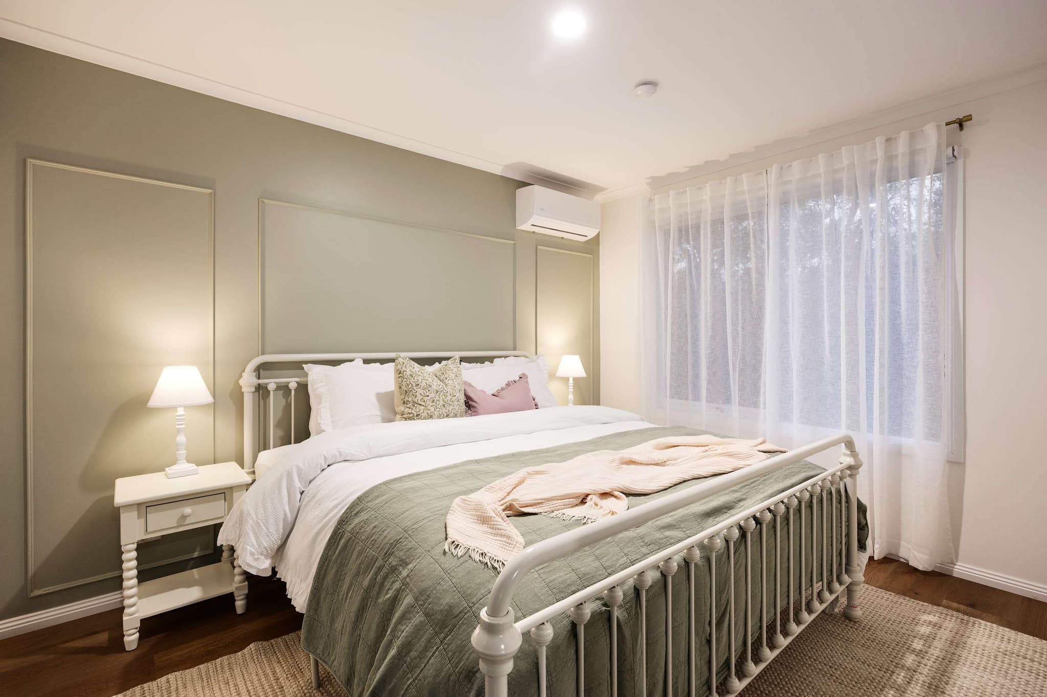 A bedroom at The Meadow with a white iron bed, sage walls and a soft green throw