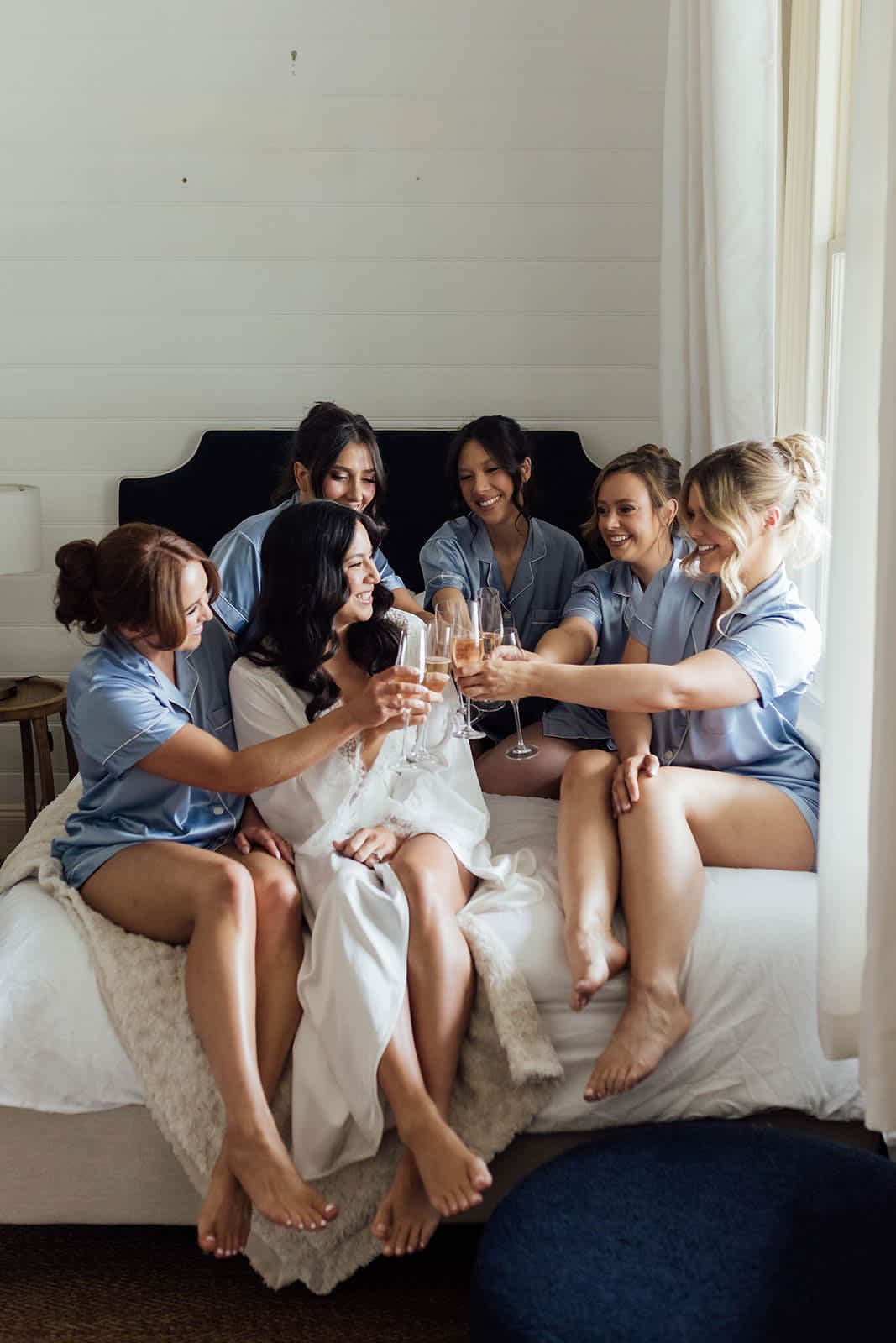 A bride and her bridesmaids toasting on a bed in matching pyjamas