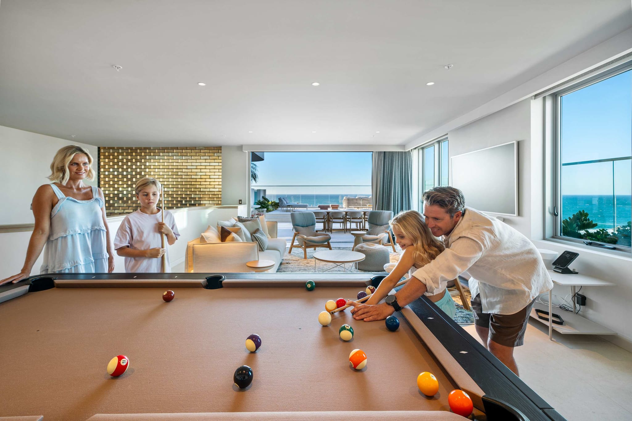 A family playing pool in the games room at RISE, with the ocean through the windows