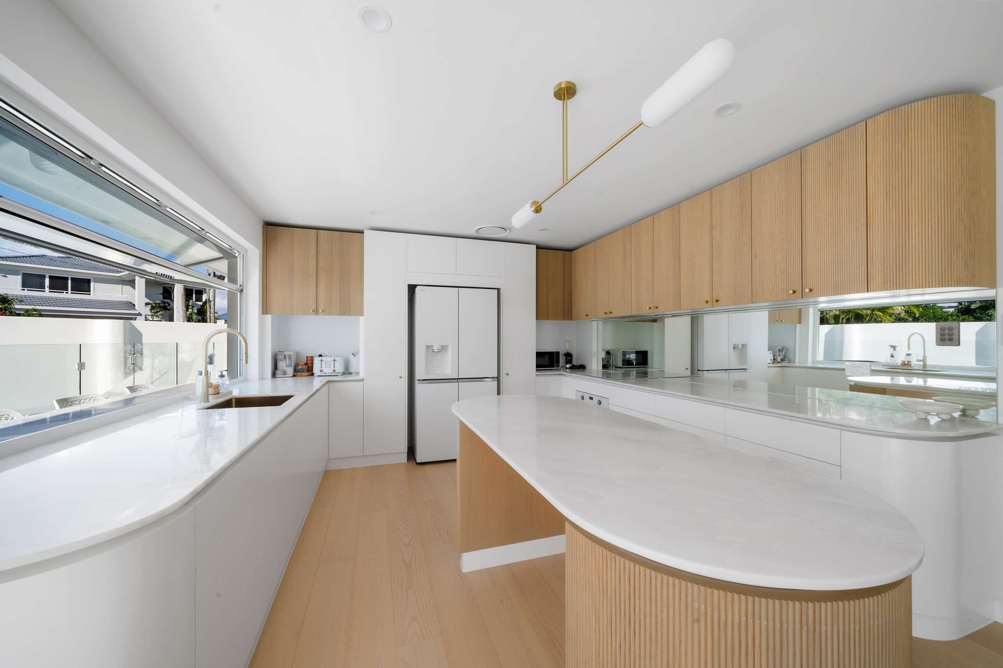 The white kitchen with timber cabinets and a curved island at The Pavilion, Mermaid Waters