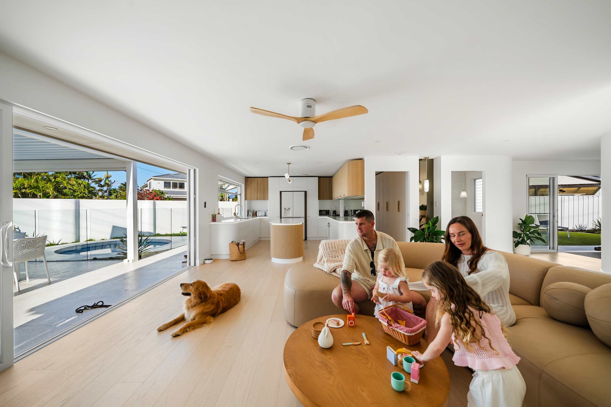 A family and their dog in the open-plan living room at The Pavilion, Mermaid Waters, with the pool through the glass