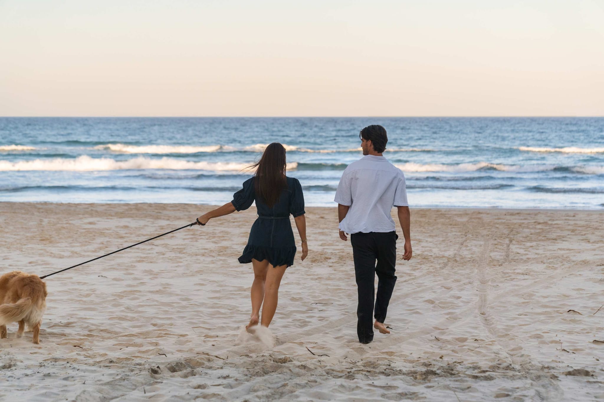 A couple walking a dog on a lead along the beach