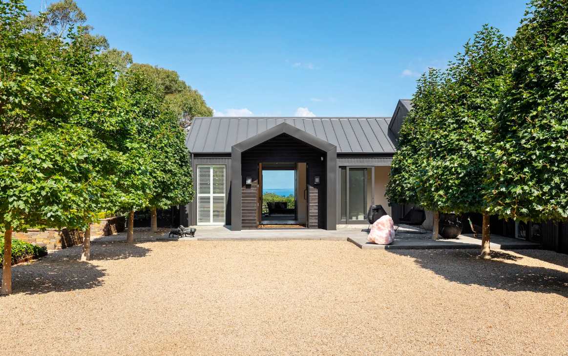 The gravel courtyard at Musk Creek between two rows of clipped trees, with the sky showing through the entry