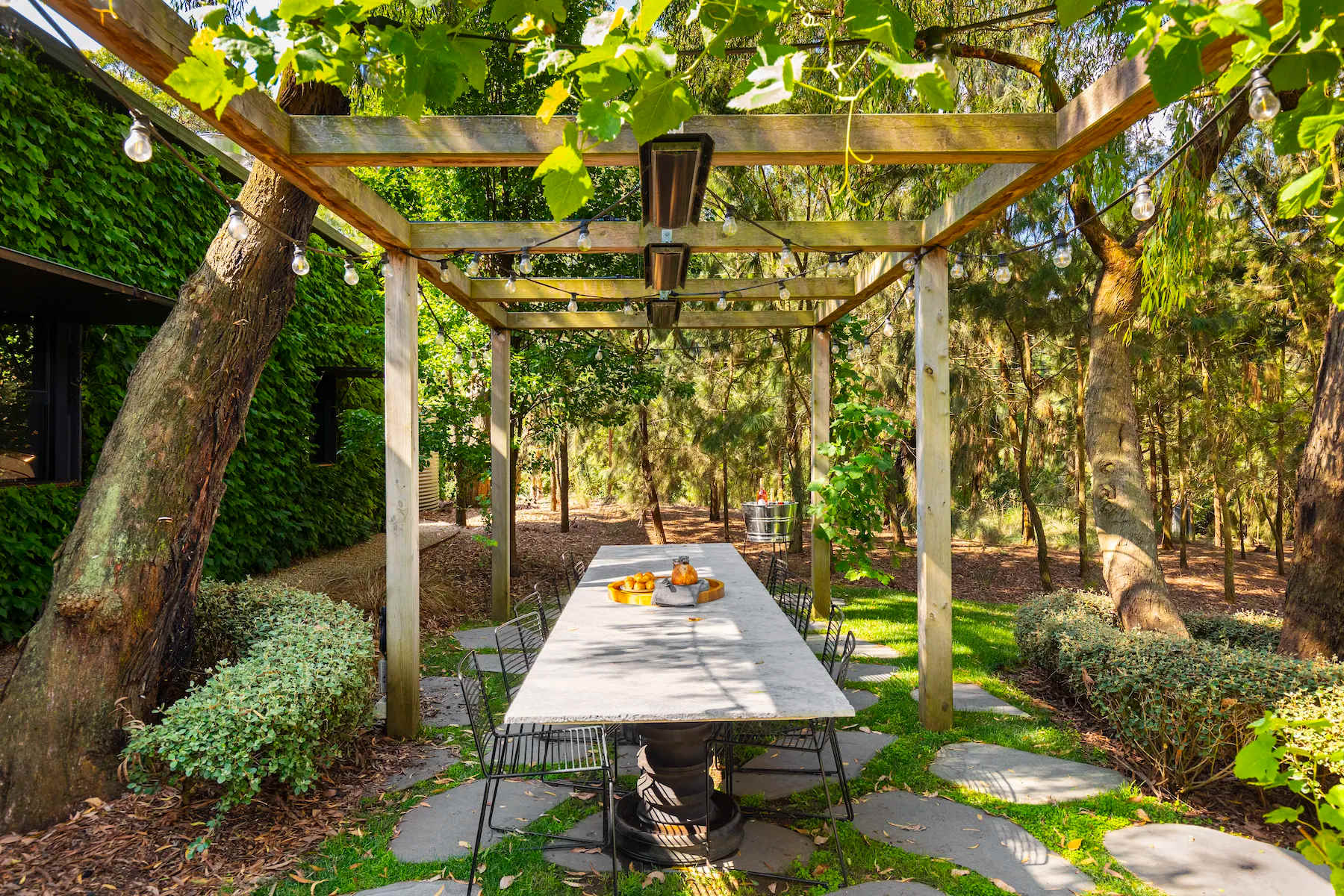 A long stone table under a vine-covered pergola among the trees at Musk Creek