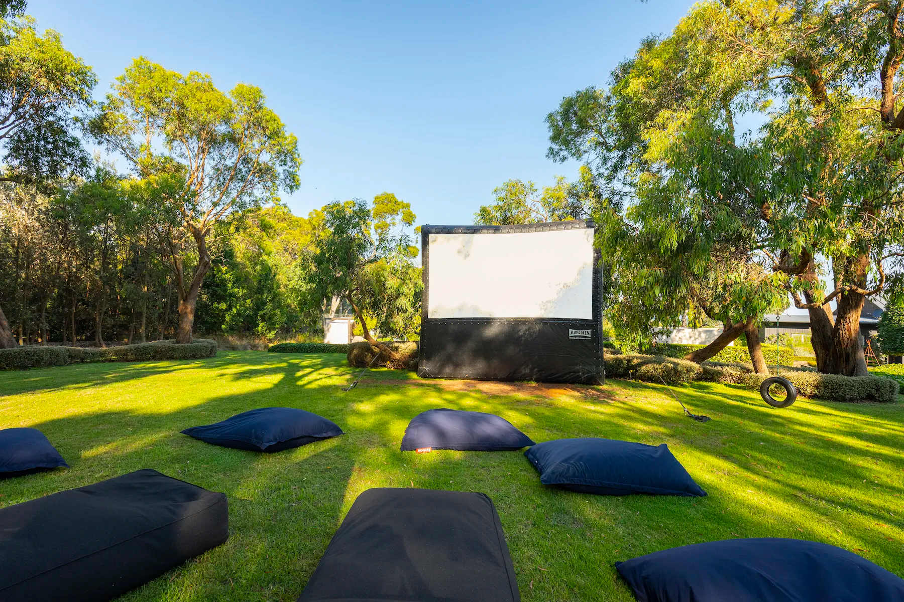 A big outdoor screen and navy bean bags on the lawn at Musk Creek under gum trees