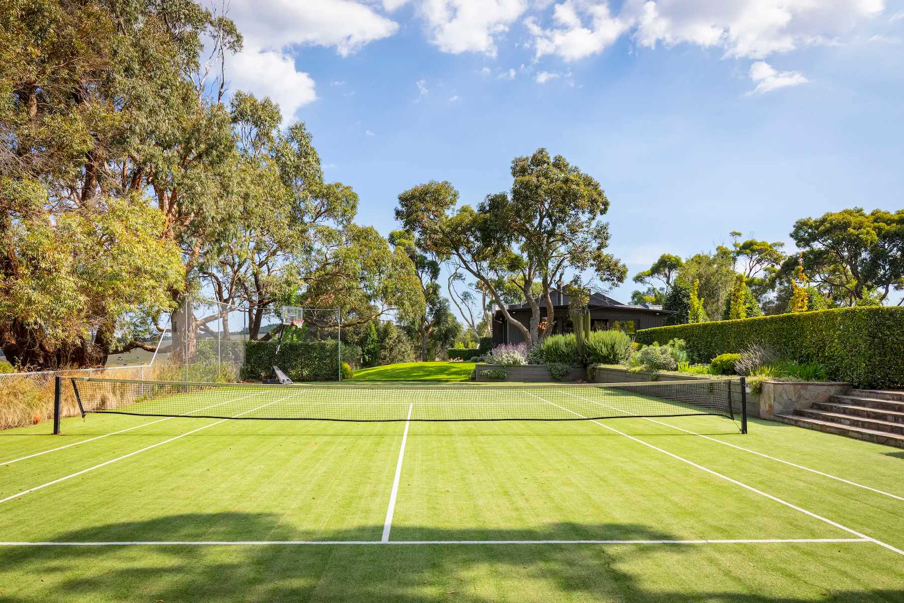 A grass tennis court at Musk Creek, framed by gum trees and clipped hedges