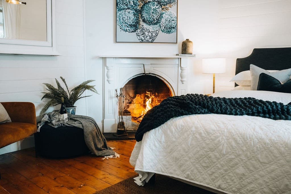 A bedroom at Oliver's Cottage with a lit open fireplace, a dark throw and polished floorboards