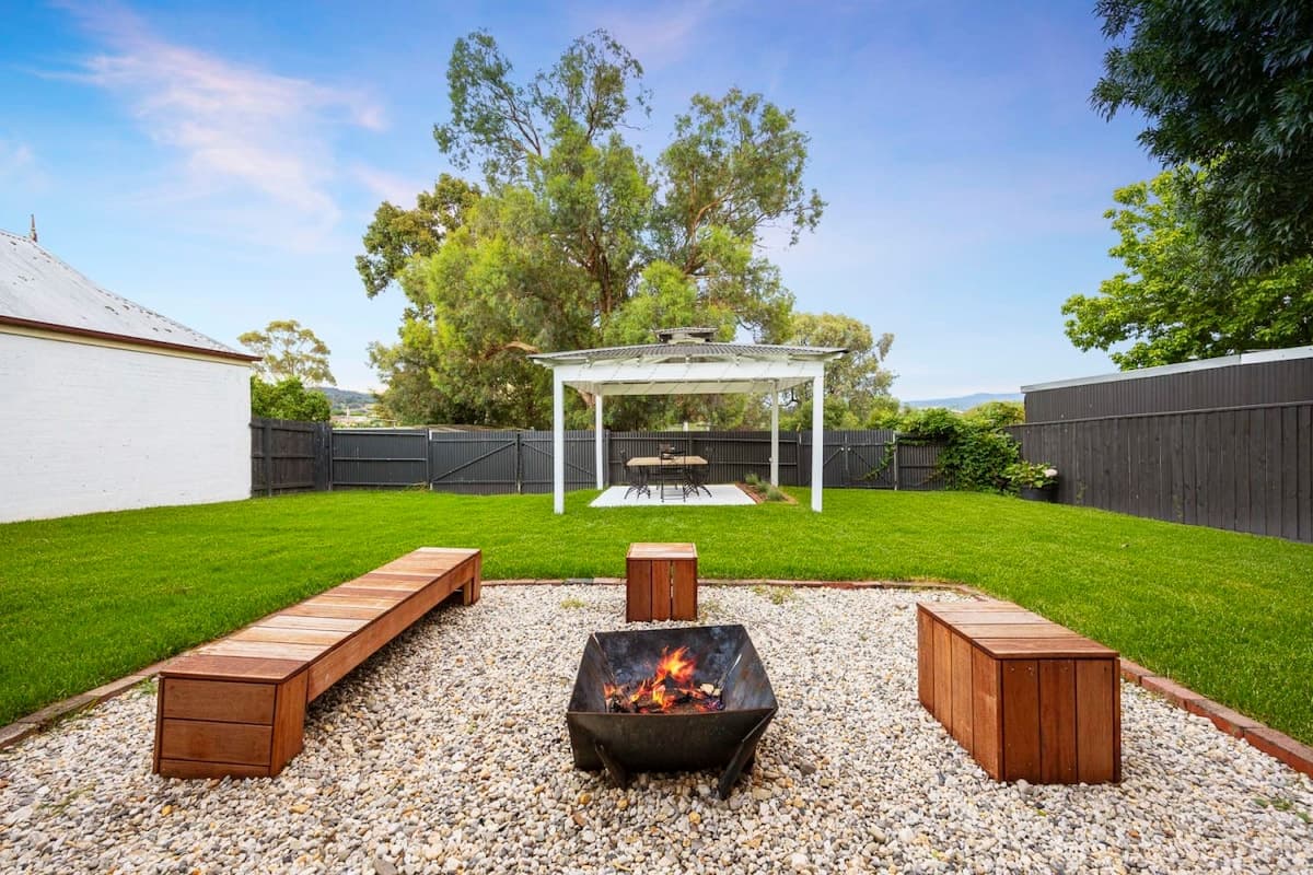 A fire pit with timber benches and a white gazebo on the lawn at Oliver's Cottage